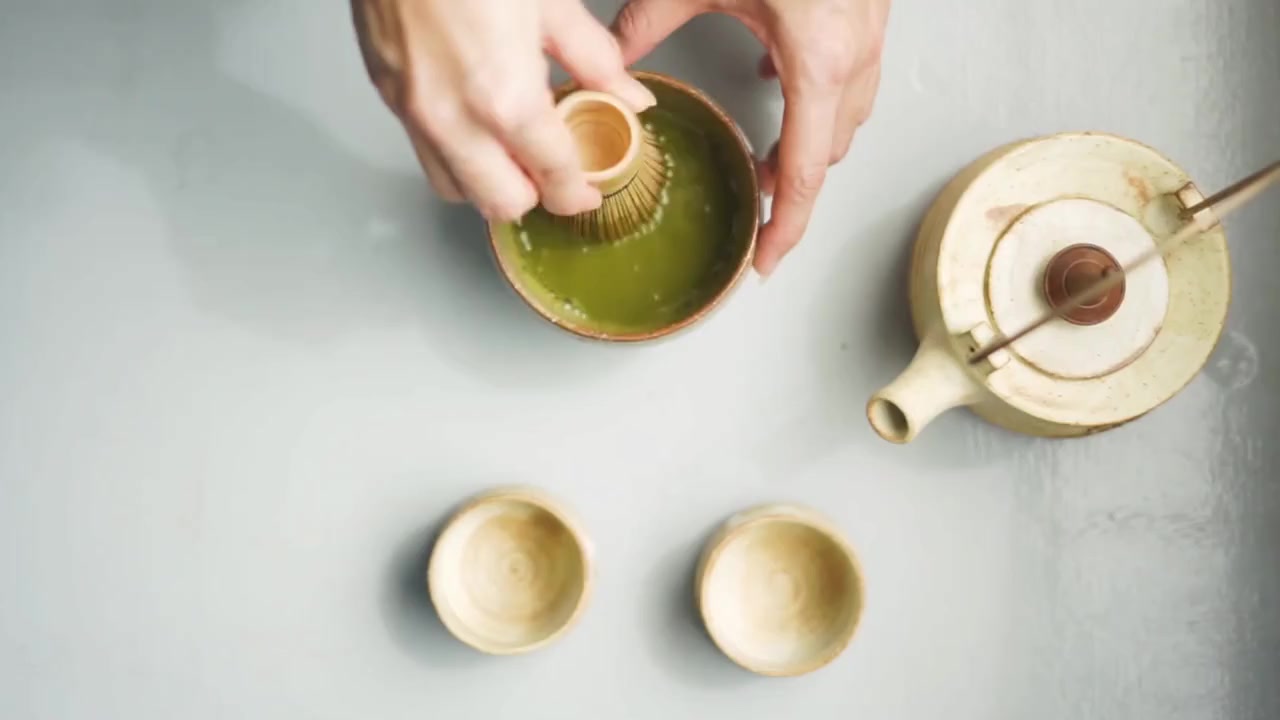 Matcha being whisked beside a ceramic teapot and cups