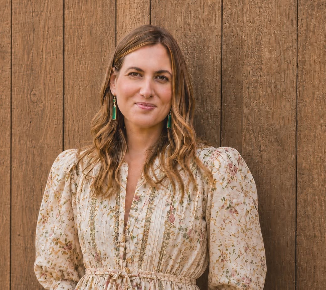 Dr. Michele Burklund in a cream floral dress standing before a carved wooden wall